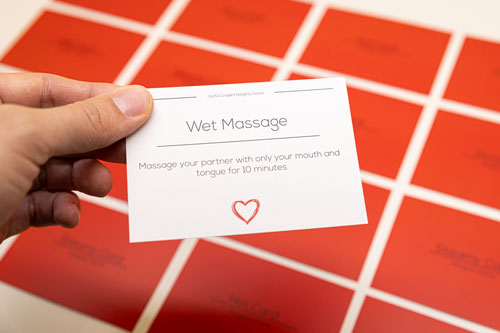 close up of a man holding one activity card of the joyful couple's naughty game in his hands