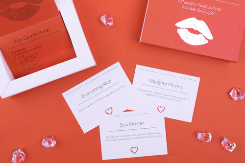 close up of some cards, box, and instruction book from the naughty game by joyful couple, red background