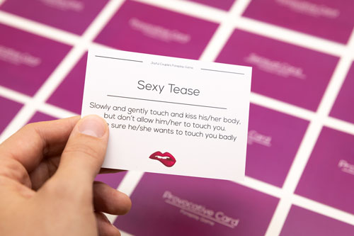 close up of a man holding one activity card in his cands from the foreplay game by joyful couple