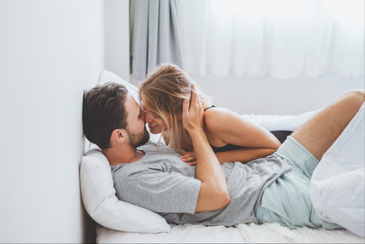 Couple cuddling on bed with soft lighting, sharing an intimate laugh before foreplay