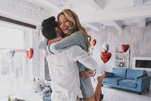 happy couple hugging, the woman is in the man's arms, white room, heart balloons in the background