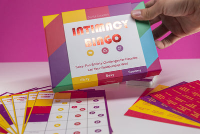 Joyful Couple's Intimacy Bingo, intimate sex card game for couples, game contents on a white and pink background, the box is held in hands