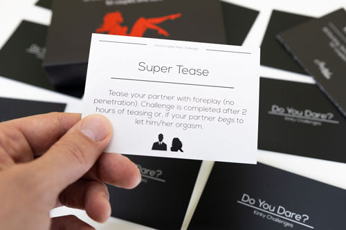close up of a man holding one activity card from kinky challenges in his hand