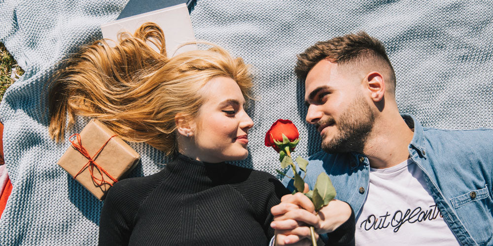 happy couple laying on the ground, the man is presenting her a rose